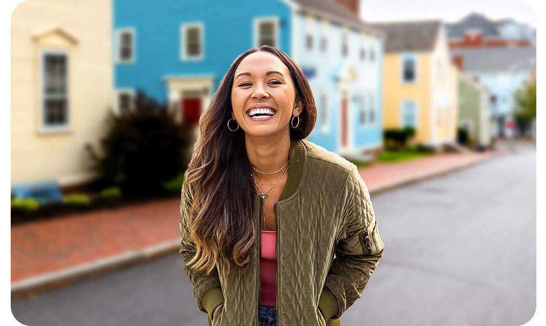 A woman is standing in front of colorful houses. However, with the Portrait On icon above activated, the background is blurred and the shot highlights the woman.