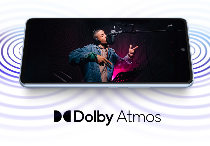 Galaxy A53 5G is laid horizontally and shows sound coming from both ends of the device. On screen, a male artist wearing headphones is singing into a studio microphone in a recording session. The Dolby Atmos logo is shown below.
