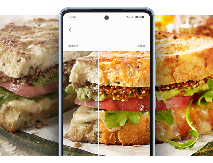A wide photo of a plate of a sliced sandwich is shown, dissected by a Galaxy A53 5G at the center. To the left of the smartphone, the image of the sandwich is bland and muted. To the right, the other half of the sandwich is shown much more bright, colorful and appetizing. On screen, the sandwich is also dissected by the Before and After effects of photo Remaster, showing the difference in image quality.