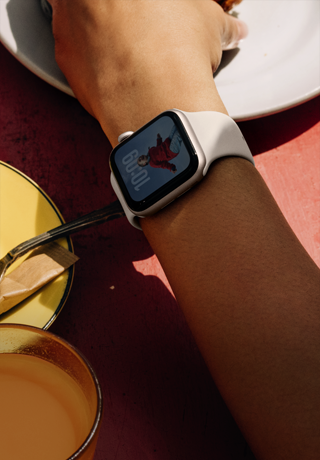 ذراع شخص يتناول الفطور وعلى معصمه Apple Watch SE 3‏ بإطار من الألومنيوم ولون ضوء النجوم، وشاشة بميزة "التشغيل دوماً"، وواجهة الساعة تحمل صورة بورتريه، وحزام رياضي بلون ضوء النجوم